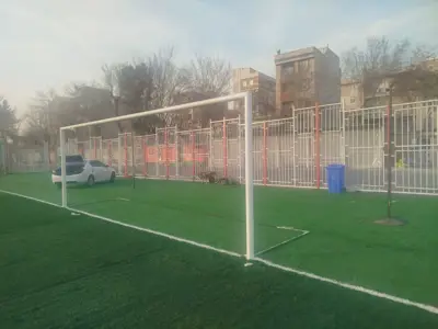 دروازه فوتبال، دروازه سفید با تور در زمین چمن مصنوعی کنار ساختمان‌ها